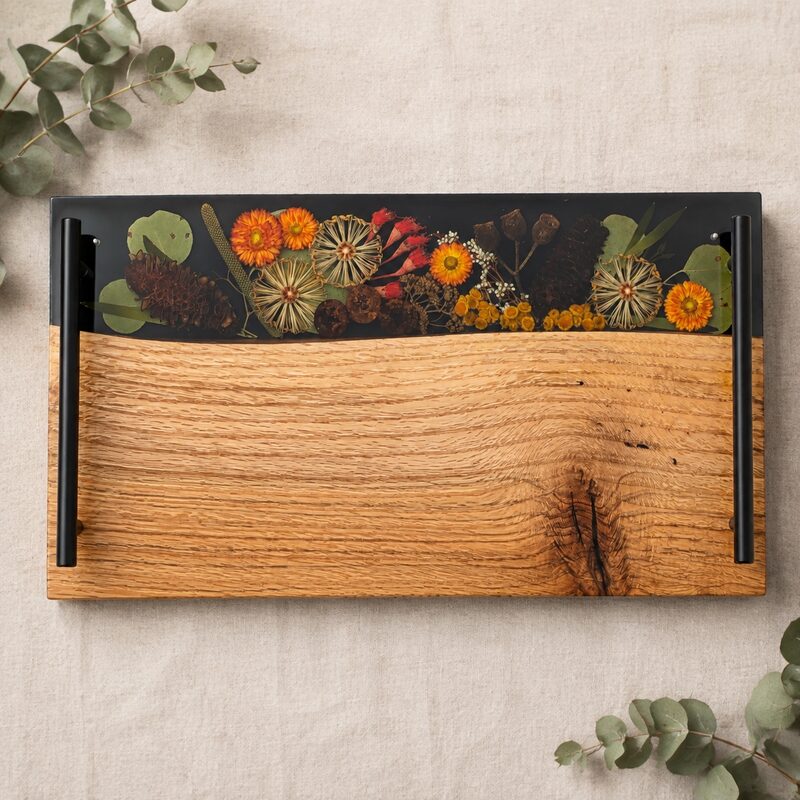 Handmade Australian timber serving board with dark resin, preserved native botanicals and black metal handles.