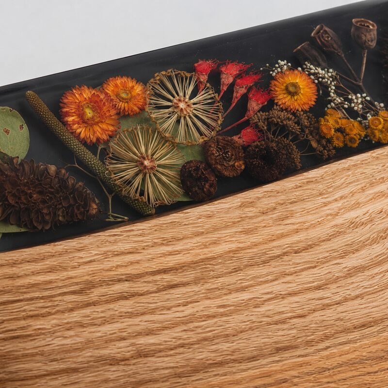 Close-up of preserved Australian botanicals encased in smooth dark resin beside natural timber grain.