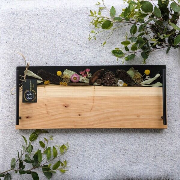 Showcasing a harmonious blend of rich wood grain and vibrant resin accents. The natural patterns of the timber are complemented by swirls of colorful resin, creating a visually striking piece. The board's ample surface area makes it perfect for arranging a variety of meats, cheeses, and accompaniments, enhancing any entertaining experience. The smooth, food-safe resin ensures easy cleaning, while the sturdy construction guarantees durability. Each charcuterie board is a unique creation, reflecting the natural variations in the wood and the artistic application of resin. This combination of functionality and aesthetic appeal makes it a standout addition to any kitchen or dining area, as well as a thoughtful gift for culinary enthusiasts.