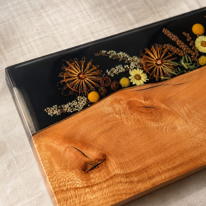 Close-up of Australian native flowers and seedpods encased beneath smooth black resin beside handcrafted golden timber.