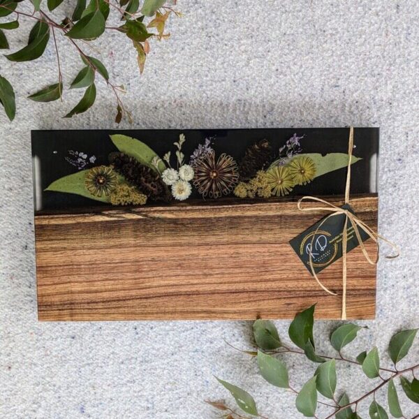 Featured in this image is a handmade charcuterie board from Resinware Designs, showcasing a harmonious blend of rich wood grain and vibrant resin accents. The natural patterns of the timber are complemented by swirls of colorful resin, creating a visually striking piece. The board's ample surface area makes it perfect for arranging a variety of meats, cheeses, and accompaniments, enhancing any entertaining experience. The smooth, food-safe resin ensures easy cleaning, while the sturdy construction guarantees durability. Each charcuterie board is a unique creation, reflecting the natural variations in the wood and the artistic application of resin. This combination of functionality and aesthetic appeal makes it a standout addition to any kitchen or dining area, as well as a thoughtful gift for culinary enthusiasts.