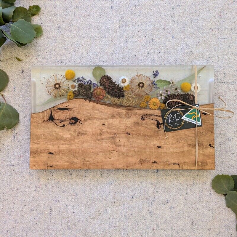 Elevate your home or gift-giving experience with our 100% Australian-made handcrafted serving board, a masterpiece of timber, resin, and dried native flora. Each board is meticulously crafted to not only serve as a functional piece but also as a captivating storyteller of the Australian bush. Experience the charm and craftsmanship of our 100% Australian-made serving board today. Order now and bring home a piece of the Australian bush that tells a story of artistry, sustainability, and natural beauty.