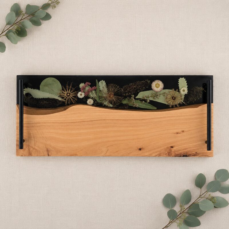 Large Australian timber and dark resin serving board with black handles and preserved native botanicals, displayed on neutral linen