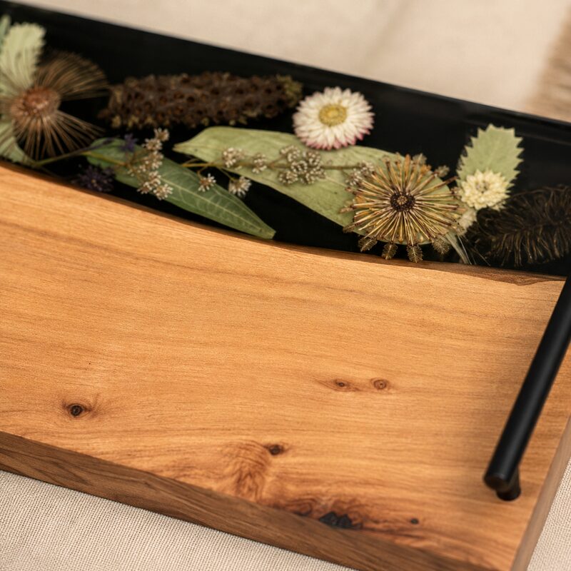 Close-up of Australian native botanicals encased beneath smooth dark resin beside natural timber grain and a black handle.