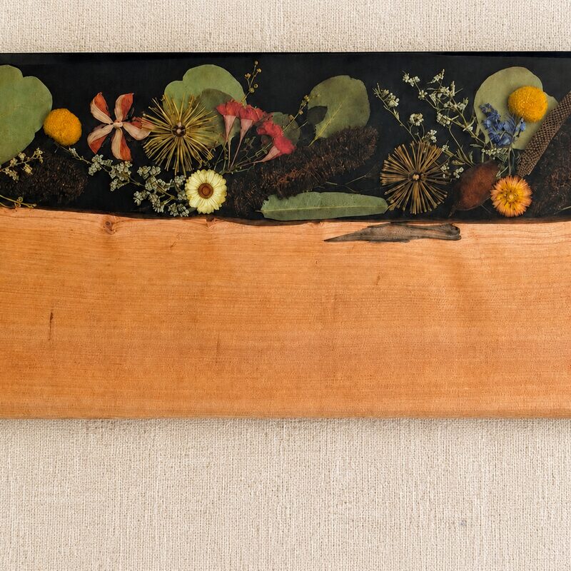 Close-up of orange flowering gum, native botanicals and natural timber encased beneath dark resin.