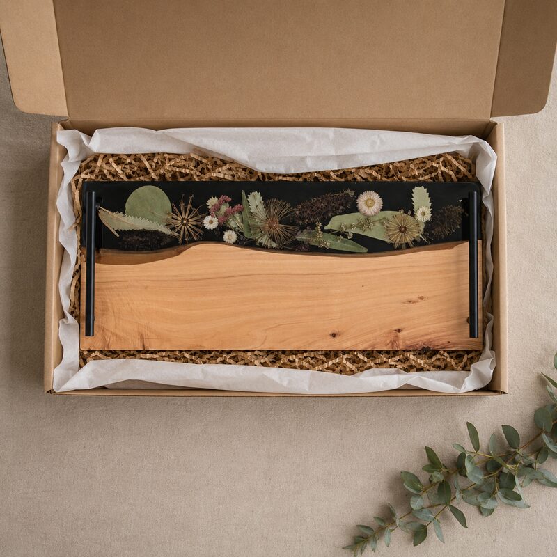 Gift presentation Australian timber and botanical resin serving board with black handles presented inside an open kraft gift box.