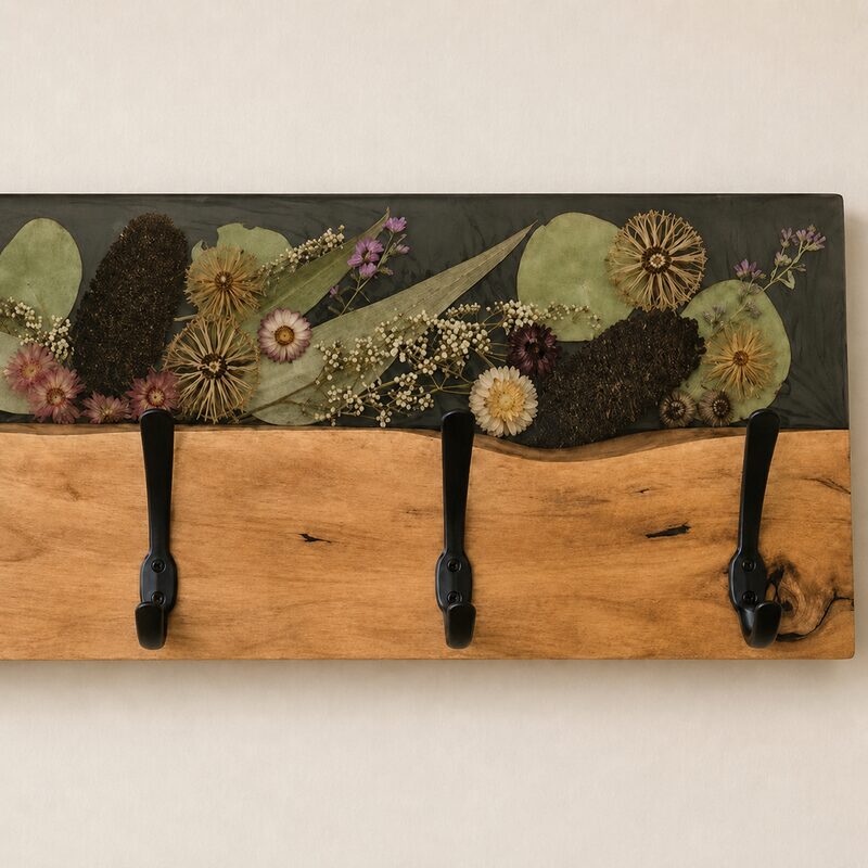 Close-up of preserved native botanicals in charcoal resin, natural timber grain and matte-black coat hooks.