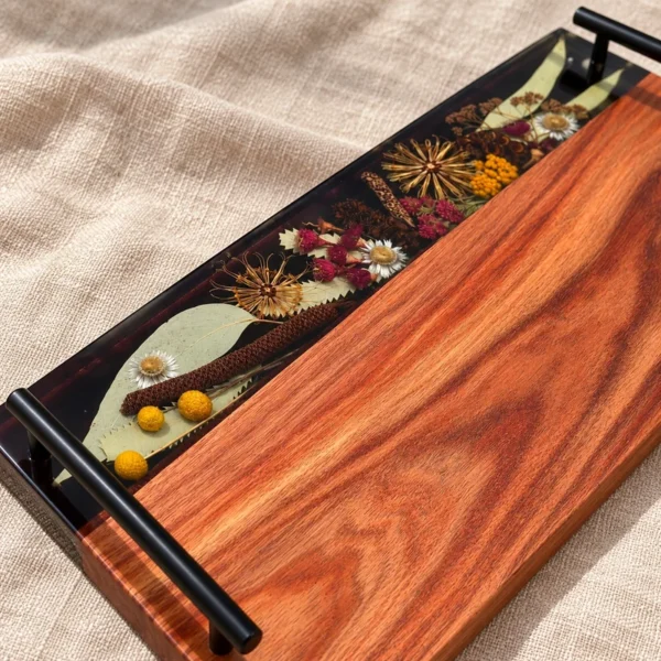 Close-up of eucalyptus leaves, yellow billy buttons and dried flowers preserved in dark resin beside rich timber grain.